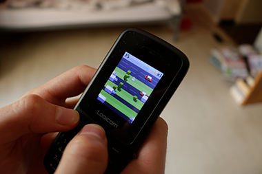 Une photo d'un téléphone mobile simple. Sur l'écran, un jeu montre une poule prête à traverser une route.